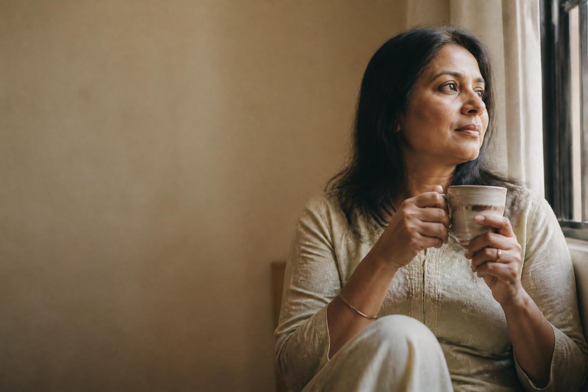 A woman sitting quietly by a window with a cup of tea in the early morning light