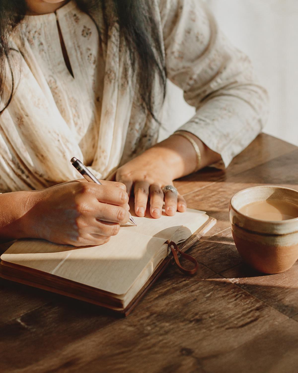 A woman writing quietly in a notebook beside a cup of tea